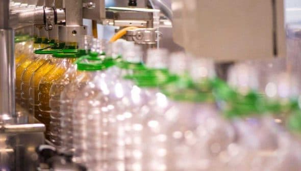 A production line with clear plastic bottles being filled with olive oil at a bottling facility. - Olive Oil Times