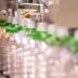 A production line with clear plastic bottles being filled with olive oil at a bottling facility. - Olive Oil Times