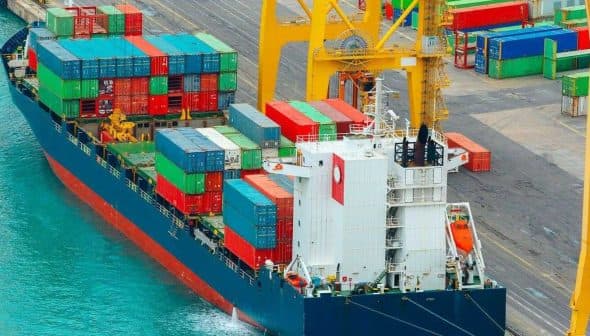 Cargo ship with colorful shipping containers docked at a port. - Olive Oil Times