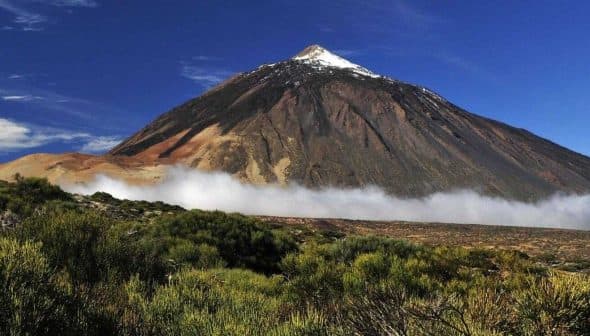 Mount Teide, a prominent volcano in Tenerife, with a snow-capped peak and surrounding clouds. - Olive Oil Times