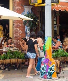 People dining outside at a restaurant with umbrellas and a brick facade on a street. - Olive Oil Times