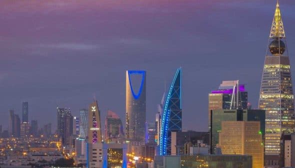 Skyline of Riyadh featuring modern skyscrapers illuminated at dusk with a purple sky. - Olive Oil Times