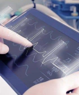 Healthcare professional interacting with a tablet displaying heart rate and vital signs data. - Olive Oil Times