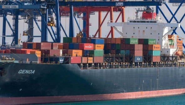 Container ship named Genoa loaded with colorful shipping containers at a port. - Olive Oil Times