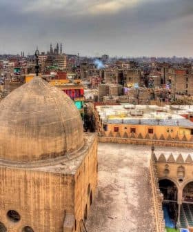 View of a historic mosque dome with a cityscape of Cairo in the background during sunset. - Olive Oil Times