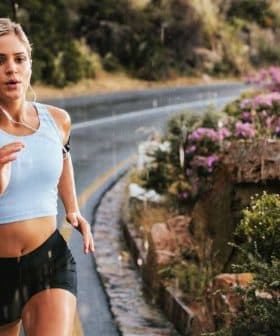 A woman jogging on a winding road with greenery and flowers along the side. - Olive Oil Times