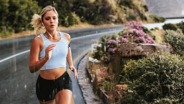 A woman jogging on a winding road with greenery and flowers along the side. - Olive Oil Times