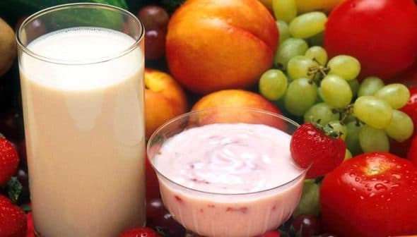 A glass of milk and a bowl of yogurt surrounded by various fruits and vegetables. - Olive Oil Times
