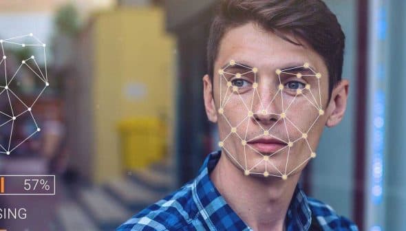 Young man with facial recognition overlay and processing indicator on his face while looking at a device. - Olive Oil Times