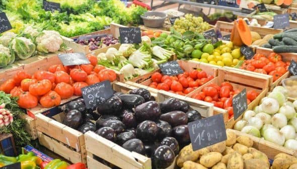 Assorted fresh vegetables displayed in wooden crates at a market stall, including tomatoes, cucumbers, and eggplants. - Olive Oil Times