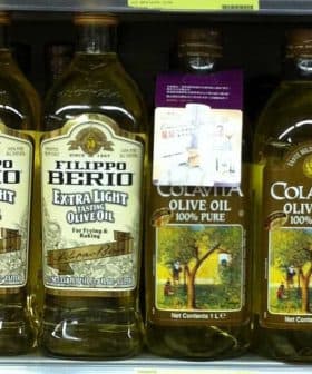 Various bottles of olive oil displayed on a supermarket shelf, including Filippo Berio and Colavita brands. - Olive Oil Times