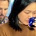 Woman with black hair holding a blue glass to her lips while tasting. - Olive Oil Times