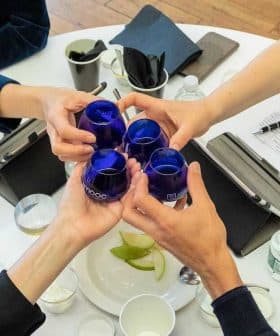 Four individuals toasting with blue glasses at a round table during a meeting. - Olive Oil Times