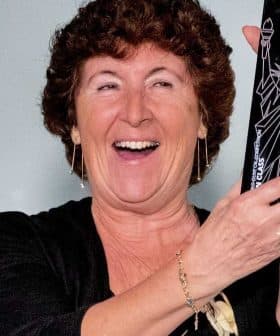 A woman with curly hair smiling while holding a black award trophy in her hands. - Olive Oil Times