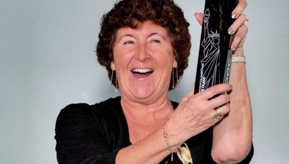 A woman with curly hair smiling while holding a black award trophy in her hands. - Olive Oil Times