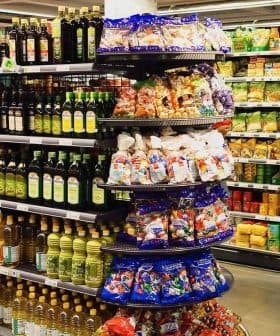 A grocery store aisle featuring shelves stocked with various olive oil bottles and snack items. - Olive Oil Times
