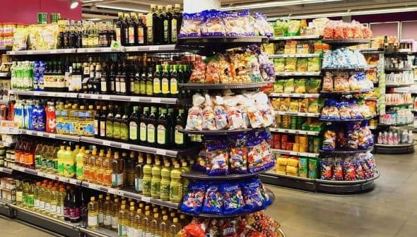 A grocery store aisle featuring shelves stocked with various olive oil bottles and snack items. - Olive Oil Times