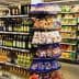A grocery store aisle featuring shelves stocked with various olive oil bottles and snack items. - Olive Oil Times