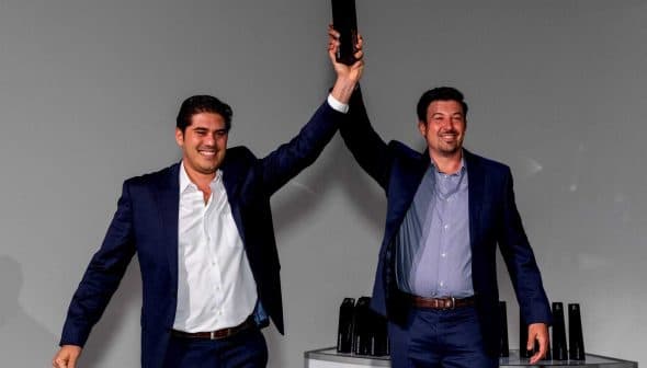 Two men in suits raising a trophy above their heads in a celebratory manner. - Olive Oil Times