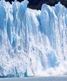 Large glacier with ice breaking off and falling into the water, creating a splash. - Olive Oil Times