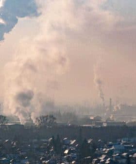Smoke rising from industrial chimneys in an urban area with a hazy sky. - Olive Oil Times