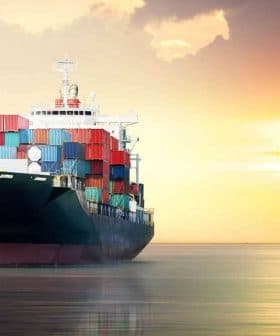 Cargo ship loaded with containers sailing on water during sunset with colorful sky. - Olive Oil Times