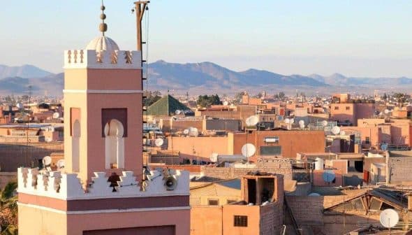 View of Marrakech cityscape featuring a prominent minaret and surrounding buildings under a clear sky. - Olive Oil Times