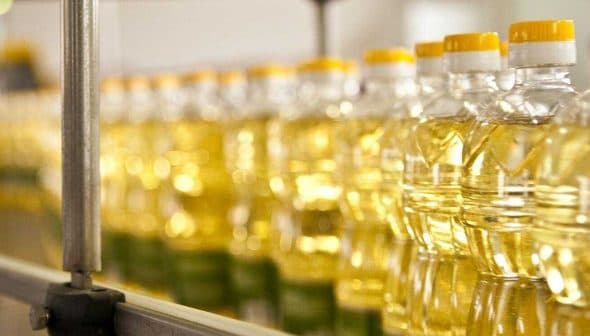 Row of clear plastic bottles filled with vegetable oil on a production line. - Olive Oil Times