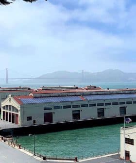 Historic waterfront buildings near the Golden Gate Bridge with water in the foreground and hills in the background. - Olive Oil Times