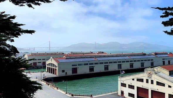 Historic waterfront buildings near the Golden Gate Bridge with water in the foreground and hills in the background. - Olive Oil Times