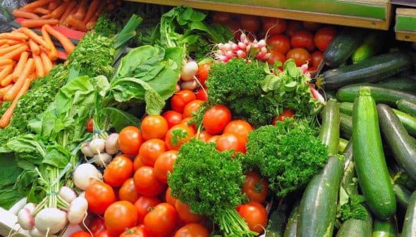 A variety of fresh vegetables including carrots, tomatoes, spinach, and zucchini arranged in a market display. - Olive Oil Times