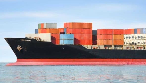 Large container ship with stacked colorful cargo containers on the deck in calm waters. - Olive Oil Times