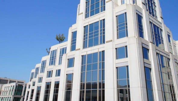 A modern building with a glass facade and geometric design, featuring multiple windows and a pointed top. - Olive Oil Times