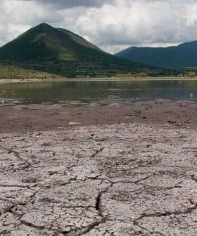 Dry, cracked earth with a mountain in the background under a cloudy sky. - Olive Oil Times
