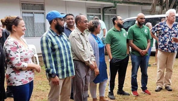 A group of diverse individuals standing together outdoors, wearing casual clothing and engaged in conversation. - Olive Oil Times