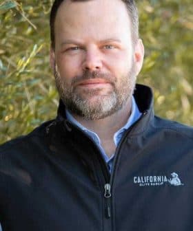 Man with a beard wearing a black vest featuring the California Olive Ranch logo. - Olive Oil Times