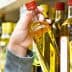 A person holding a bottle of olive oil from a shelf in a grocery store. - Olive Oil Times