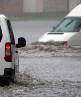 Two vehicles navigating through a flooded street during heavy rain. - Olive Oil Times
