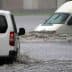 Two vehicles navigating through a flooded street during heavy rain. - Olive Oil Times