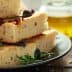 Slices of focaccia bread topped with olives and herbs on a black plate. - Olive Oil Times