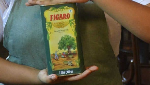 Person holding a green Figaro brand olive oil container with a tree illustration on the label. - Olive Oil Times