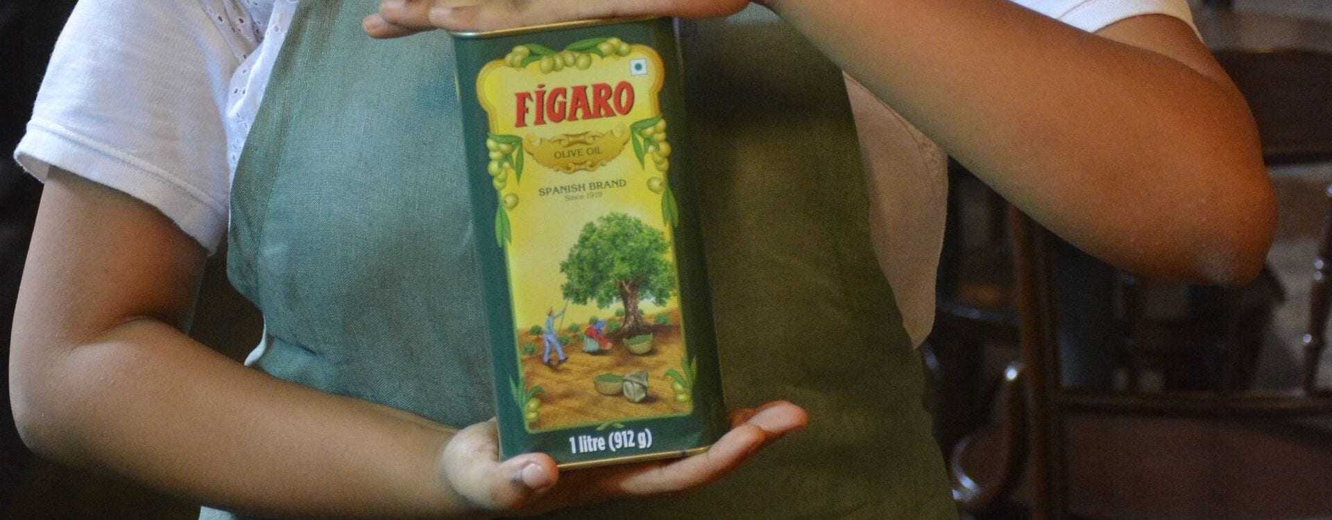 Person holding a green Figaro brand olive oil container with a tree illustration on the label. - Olive Oil Times