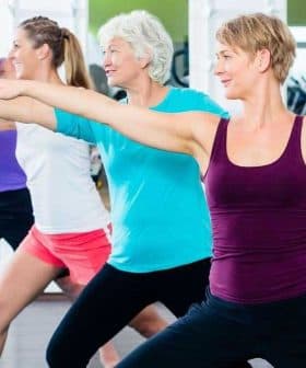 Four adults performing a fitness exercise in a gym setting with arms extended. - Olive Oil Times