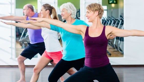Four adults performing a fitness exercise in a gym setting with arms extended. - Olive Oil Times