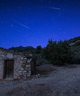 A stone building with a wooden door under a starry night sky with visible meteor trails. - Olive Oil Times