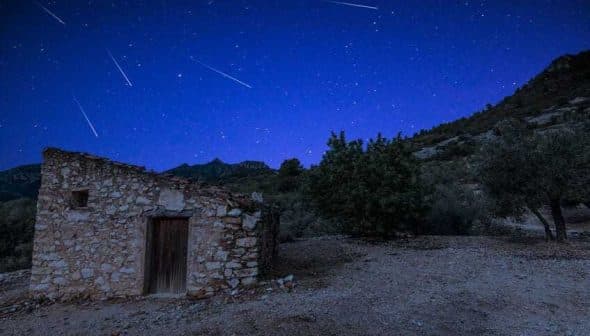 A stone building with a wooden door under a starry night sky with visible meteor trails. - Olive Oil Times