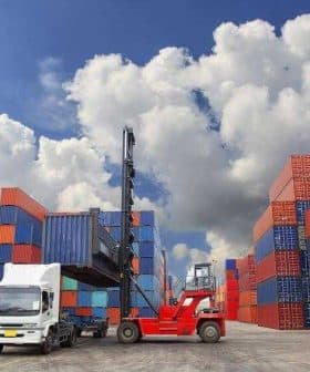 A forklift lifting a shipping container in a storage area surrounded by stacked containers. - Olive Oil Times