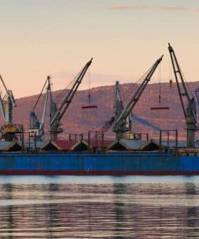 Cargo ship docked at the port of Volos with cranes and a tugboat nearby. - Olive Oil Times