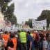 Crowd of protesters wearing orange vests holding banners regarding olive oil prices. - Olive Oil Times