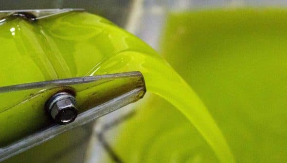 Stream of bright green extra virgin olive oil flowing from a mill spout into a container. - Olive Oil Times